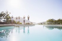 Giovani persone attraenti che praticano yoga a bordo piscina — Foto stock