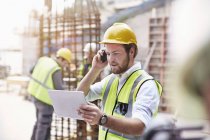 Ingénieur avec tablette numérique parlant sur un téléphone portable sur le chantier de construction — Photo de stock