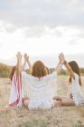 Boho women sitting in circle with arms raised and connected in rural field — Stock Photo