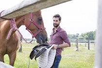 Man removing saddle from horse in rural pasture — Stock Photo
