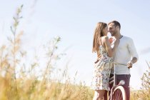 Affectionate young couple with bike hugging in sunny rural field — Stock Photo