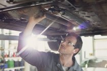 Mechaniker arbeitet unter Auto in Autowerkstatt — Stockfoto