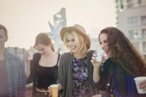Sonrientes mujeres jóvenes bebiendo y riendo en la fiesta en la azotea - foto de stock
