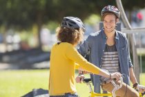 Man and woman with bicycles wearing helmets and talking in park — Stock Photo