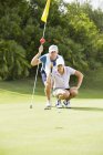 Caddy caucasiano e golfista se preparando para putt — Fotografia de Stock