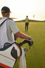 Rear view of golfer and caddy nearing golf flag — Stock Photo