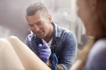 Tattoo artist tattooing woman leg at studio — Stock Photo