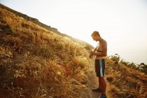 Bare chested male runner on trail checking smart watch — Stock Photo