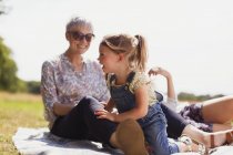 Бабуся і онука сміються на ковдрі в сонячному полі — стокове фото