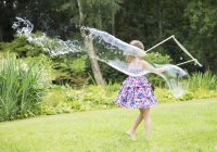 Chica haciendo grandes burbujas en el patio trasero - foto de stock