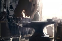 Blacksmith at fire behind anvil in forge — Stock Photo