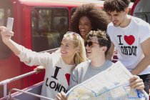 Friends with map taking selfie on double-decker bus — Stock Photo