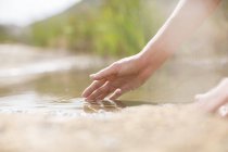 Mujer sumergiendo dedos en estanque rural - foto de stock