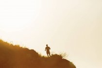 Силуэт человека, бегущего по холму на закате — стоковое фото