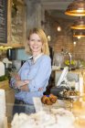 Portrait smiling cafe owner with arms crossed behind the counter — Stock Photo