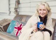 Retrato sonriente mujer mayor bebiendo café en el sofá del patio - foto de stock