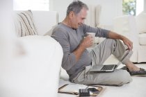 Вид збоку на старшого білого чоловіка, що сидить на підлозі з ноутбуком — стокове фото