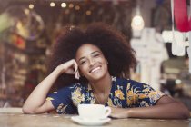 Retrato sonriente mujer con afro beber café en la cafetería - foto de stock