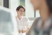 Усміхнена жінка п'є біле вино в сонячному ресторані — стокове фото