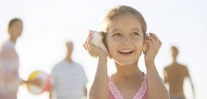 Дівчина слухає мушлі на пляжі — стокове фото