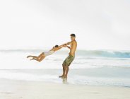 Отец размахивает дочерью на пляже — стоковое фото