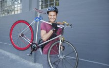 Portrait jeune homme souriant portant un vélo sur le trottoir urbain — Photo de stock