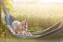 Gelassene Seniorin liegt in Hängematte neben ländlichem Weizenfeld — Stockfoto