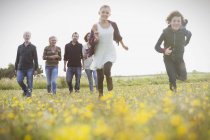 Energetic brother and sister running in meadow with family in background — Stock Photo