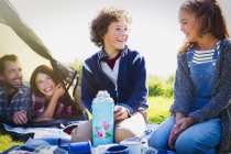 Lächelndes Geschwisterpaar mit isoliertem Getränkebehälter auf dem Campingplatz — Stockfoto
