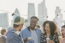 Young adult friends talking and drinking at rooftop party — Stock Photo