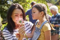 Mother and daughter smelling fresh pink flower in sunny garden — Stock Photo