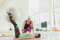 Personal trainer guiding woman with fitness ball between legs — Stock Photo