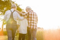 Affectionate grandparents and grandson walking along sunny rural wheat field — Stock Photo