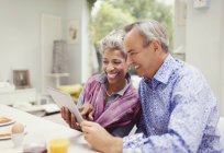 Sonriente pareja adulta compartiendo tableta digital en la mesa del desayuno - foto de stock