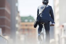 Businessman in suit and helmet riding bicycle in city — Stock Photo