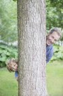 Padre e hijo mirando desde detrás del árbol - foto de stock