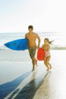 Père et fille portant planche de surf et bodyboard sur la plage — Photo de stock