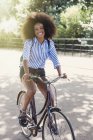 Retrato sorridente mulher com afro andar de bicicleta no parque — Fotografia de Stock