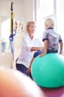 Fisioterapeuta sosteniendo chico en fitness ball - foto de stock