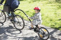 Menino andar de bicicleta em tandem com empresário pai no parque ensolarado — Fotografia de Stock