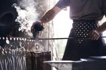 Blacksmith pouring hot liquid over wrought iron in forge — Stock Photo