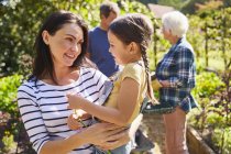 Affectionate mother holding daughter in sunny garden — Stock Photo