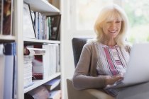 Усміхнена старша жінка використовує ноутбук у джинсі — стокове фото