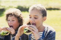 Brother and sister eating hamburgers outside — Stock Photo