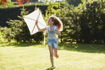 Mädchen läuft mit Drachen im sonnigen Garten — Stockfoto