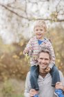 Portrait smiling father carrying toddler son on shoulders in autumn park — Stock Photo