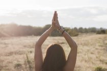 Frau meditiert mit Händen über Kopf in sonnigem, ländlichem Feld — Stockfoto