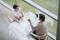 Paar stößt Weingläser am Restauranttisch am Fenster an — Stockfoto