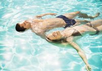 Joven pareja atractiva flotando en la piscina - foto de stock