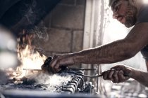 Blacksmith working over fire in forge — Stock Photo
